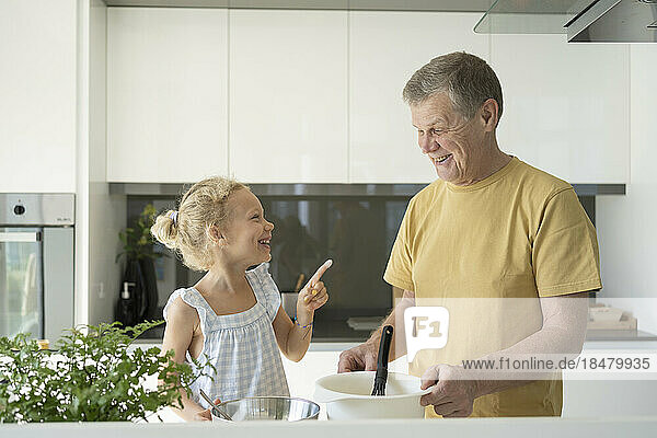 Smiling girl pointing at grandfather in kitchen