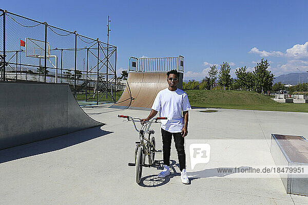 Young man standing with BMX bike at skatepark
