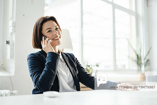 Happy businesswoman talking through mobile phone at desk in office