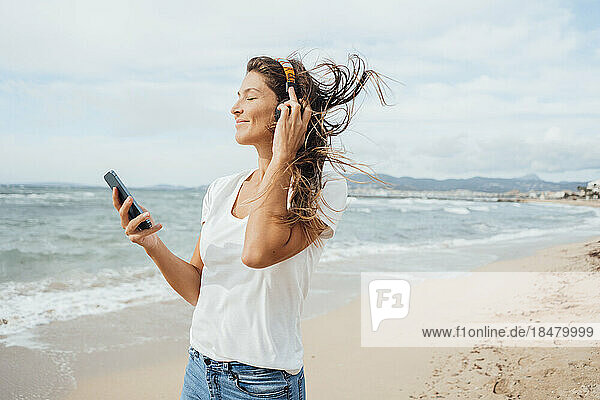 Smiling woman enjoying listening to music through headphones at beach