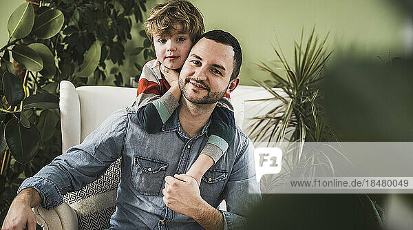 Smiling father with son sitting on armchair at home