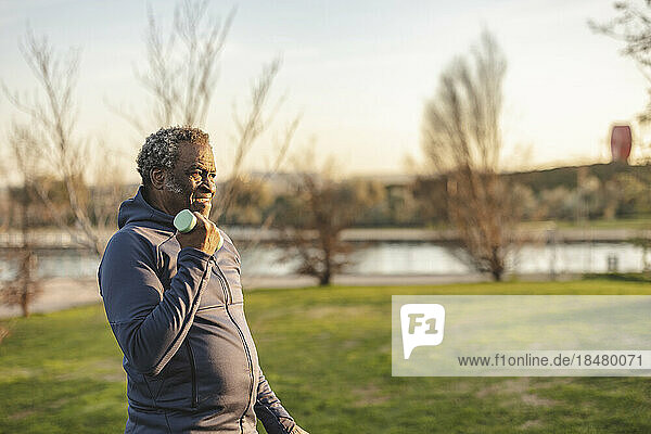 Senior man holding dumbbell exercising in park at sunset