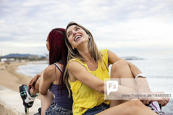 Happy woman with friend sitting back to back at promenade