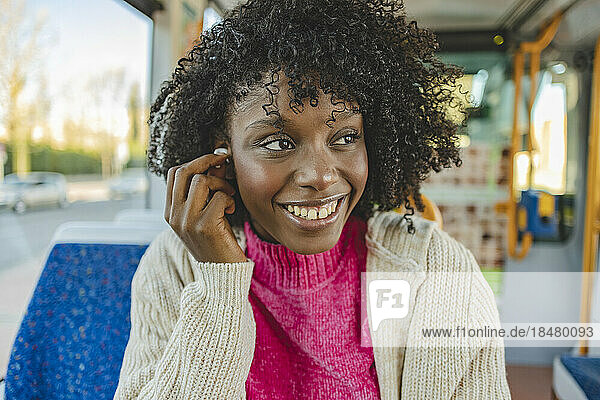 Happy woman with wireless in-ear headphones sitting in tram