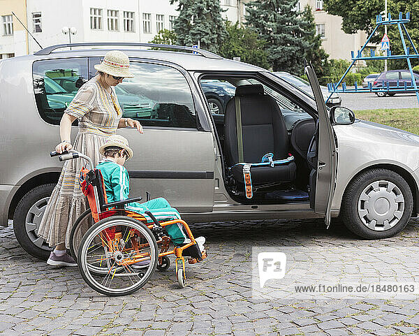 Mutter hilft Tochter  die im Rollstuhl neben Auto sitzt