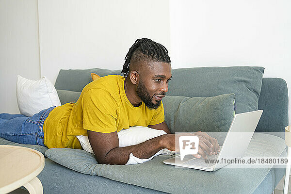 Freelancer lying on sofa and using laptop at home