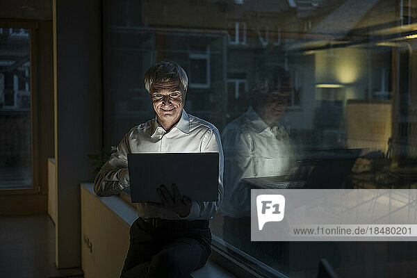 Lächelnder Geschäftsmann  der spät am Laptop im Büro arbeitet