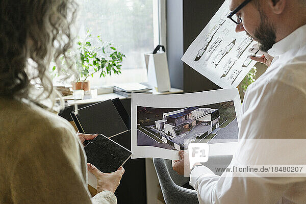 Two colleagues holding printout of a house and blueprint in architect's office