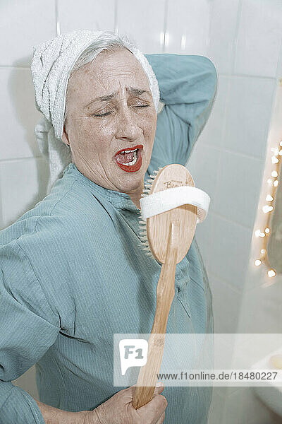 Senior woman with wooden brush singing in bathroom