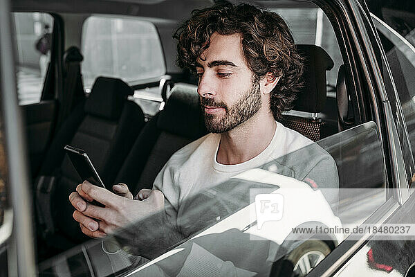 Young man using mobile phone traveling in car