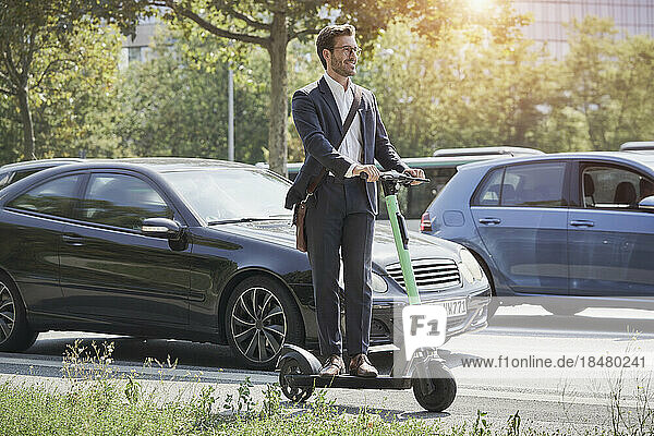 Smiling businessman standing on electric push scooter on road