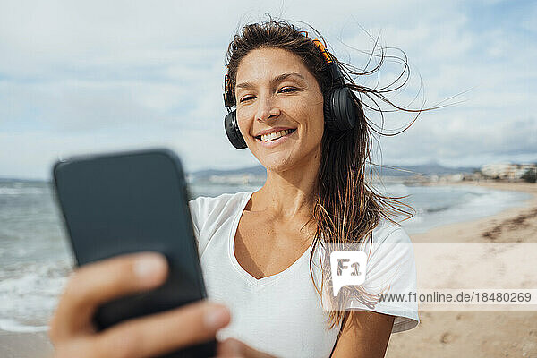 Woman wearing headphones taking selfie through smart phone at beach