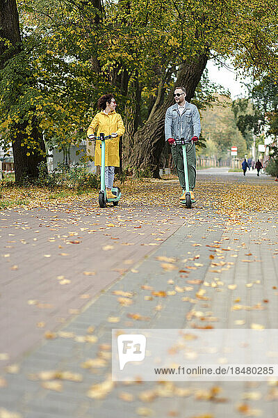 Man and woman riding electric push scooter in autumn park