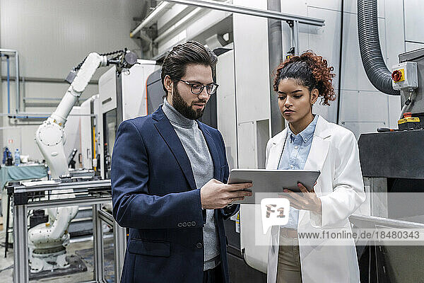 Young businessman with colleague discussing over tablet PC in factory