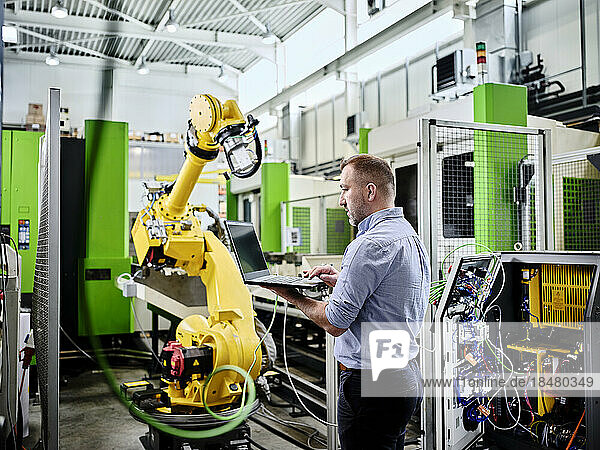 Technician using laptop at robotic arm in modern factory