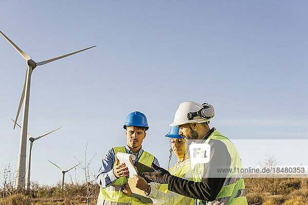 Engineers and technician discussing over document near wind turbines