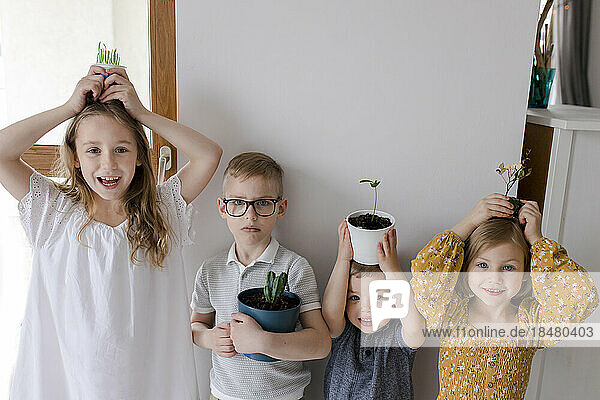 Siblings with houseplants on hands at home