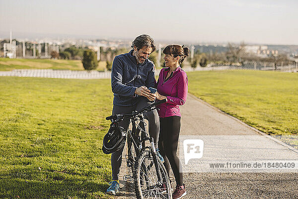 Happy couple with bicycle using smart phone in park