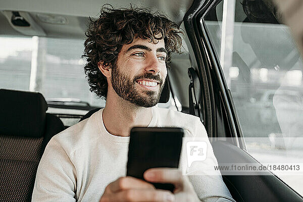 Smiling young man with smart phone sitting in car