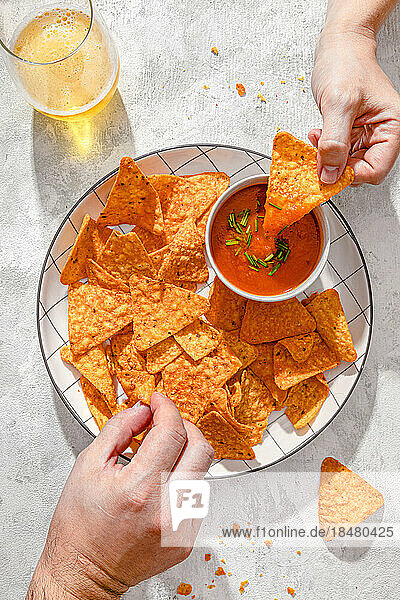Hands of man and woman holding nachos with tomato sauce