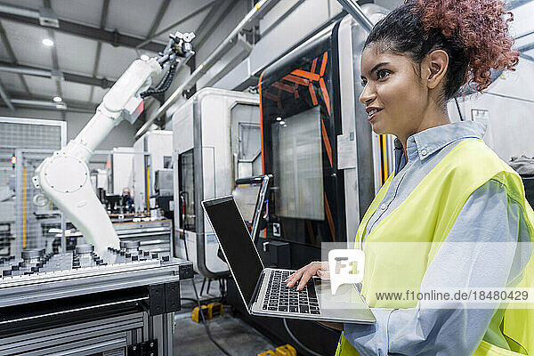 Happy young engineer standing with laptop in factory