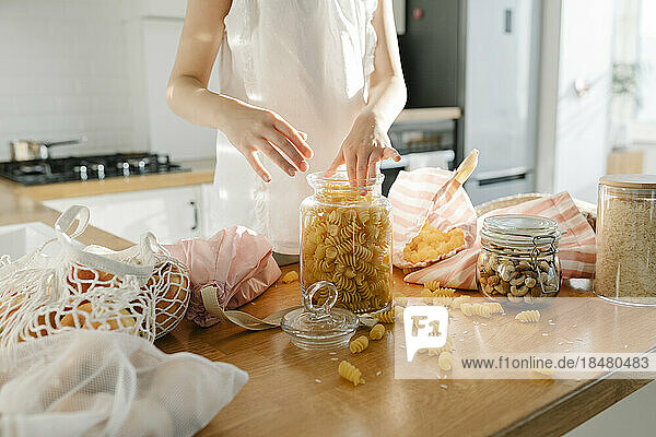 Girl with pasta in glass jar on kitchen island at home