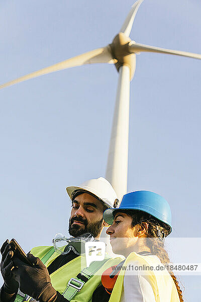 Engineer with technician using smart phone in front of wind turbine