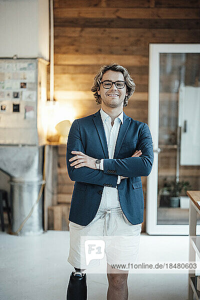 Happy young businessman with arms crossed standing in office