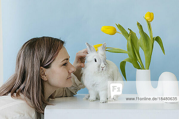 Frau streichelt Kaninchen neben Tulpenvase auf Tisch