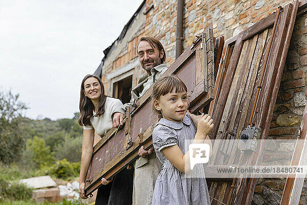 Glückliche Frau und Mann mit Tochter  die eine Holztür trägt