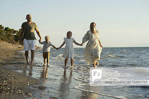 Familie geht Händchen haltend am Strand entlang