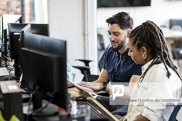Young businessman and businesswoman working on charts at desktop PC in office