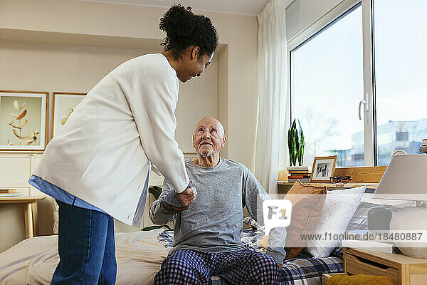 Nurse helping senior man in getting up from bed
