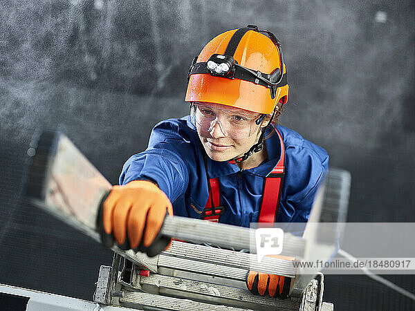 Industrial worker wearing hard hat and climbing harness ascending ladder