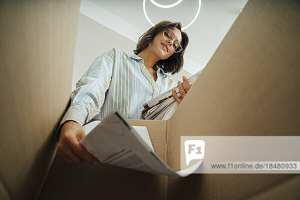 Smiling young woman recycling papers in box at home