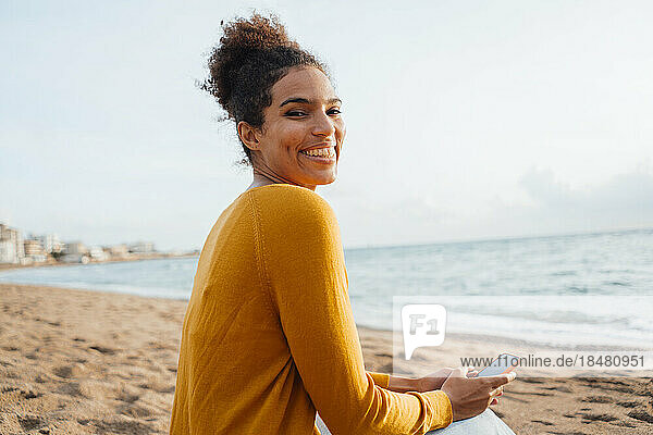 Glückliche Frau sitzt mit Handy am Strand