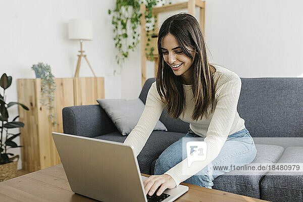 Happy young woman using laptop sitting on sofa at home