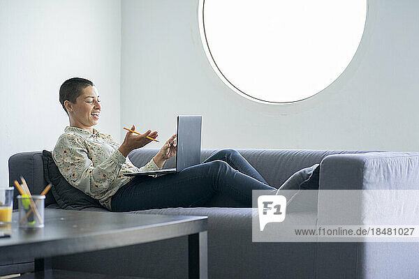 Happy businesswoman doing video call over laptop reclining on sofa at home office