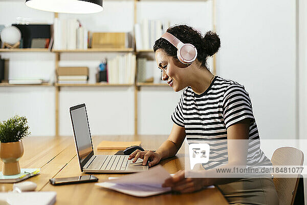 Smiling freelancer wearing wireless headphones working on laptop at table