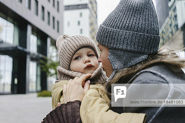Woman wearing knit hat embracing son in front of building