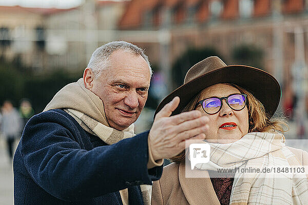Senior man gesturing by woman wearing hat and eyeglasses