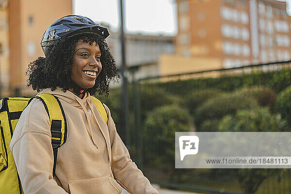 Happy delivery woman wearing helmet standing with backpack