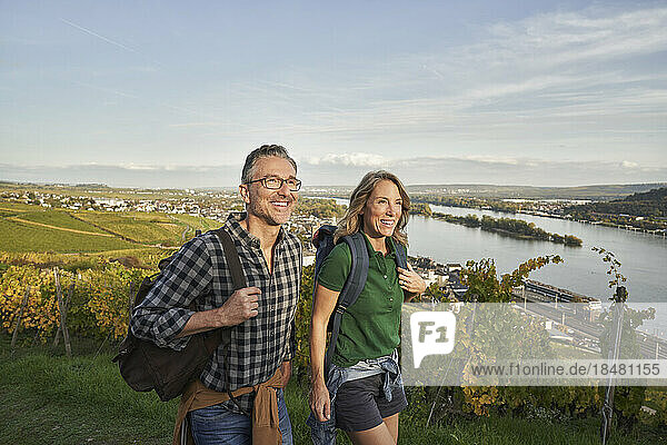 Happy mature couple hiking by vineyard under blue sky