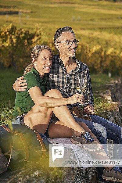 Contemplative tourists sitting with wineglasses on wall