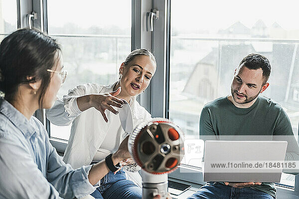 Businesswoman touching blade of wind turbine rotor in meeting with colleagues at office