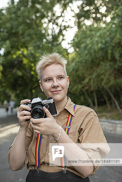 Smiling non-binary person with camera standing in park