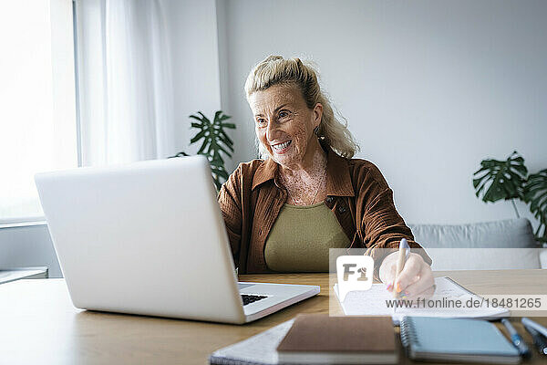 Happy elderly freelancer doing video call on laptop at home office