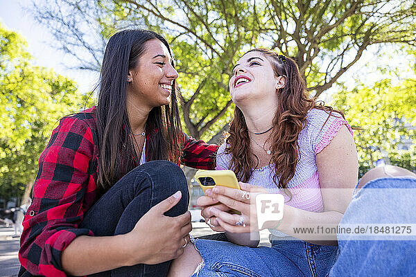 Happy woman sitting with girlfriend holding smart phone