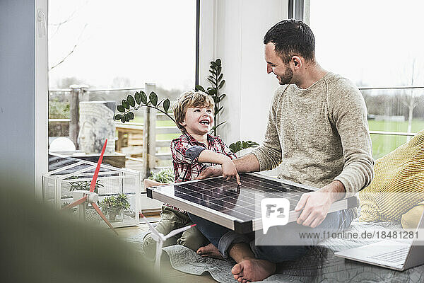 Glücklicher Sohn schaut Vater an  der zu Hause mit Solarpanel sitzt