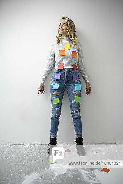 Smiling woman with colorful adhesive notes on body standing in front of wall